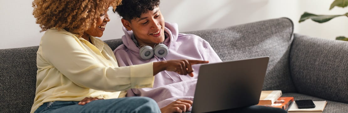 Mother and son sitting on a couch looking at a laptop computer together. 