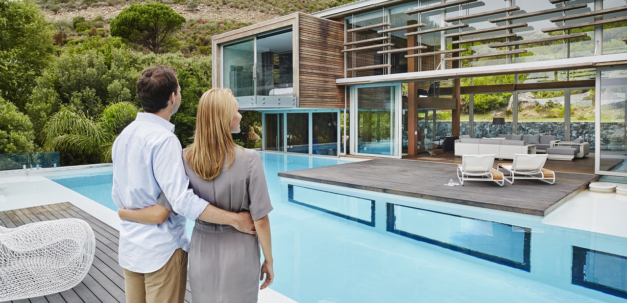 Couple standing behind their home looking at their pool and house.