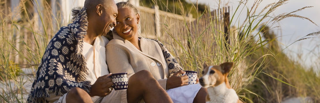 Mature couple sitting on beach with their dog outside their home.